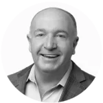 White male in his late 50's in a suit with no tie smiling for a headshot. The image is in black and white and cropped into a circle for the board and staff page of PRC's website